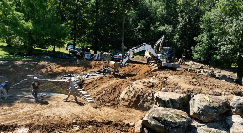 Before water can move through a natural-looking waterfall or reflect the surrounding landscape, crews have to manage excavation, soil, stone, liner, filtration components, access routes, drainage, and changing weather.