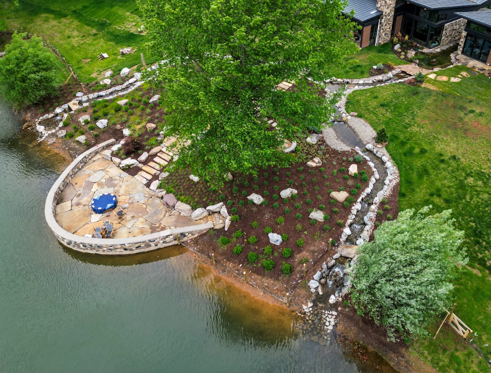 The pond begins near the front entrance, where it opens to approximately 12 feet wide and 3 feet deep, curving naturally through the landscape rather than following a rigid geometric footprint.