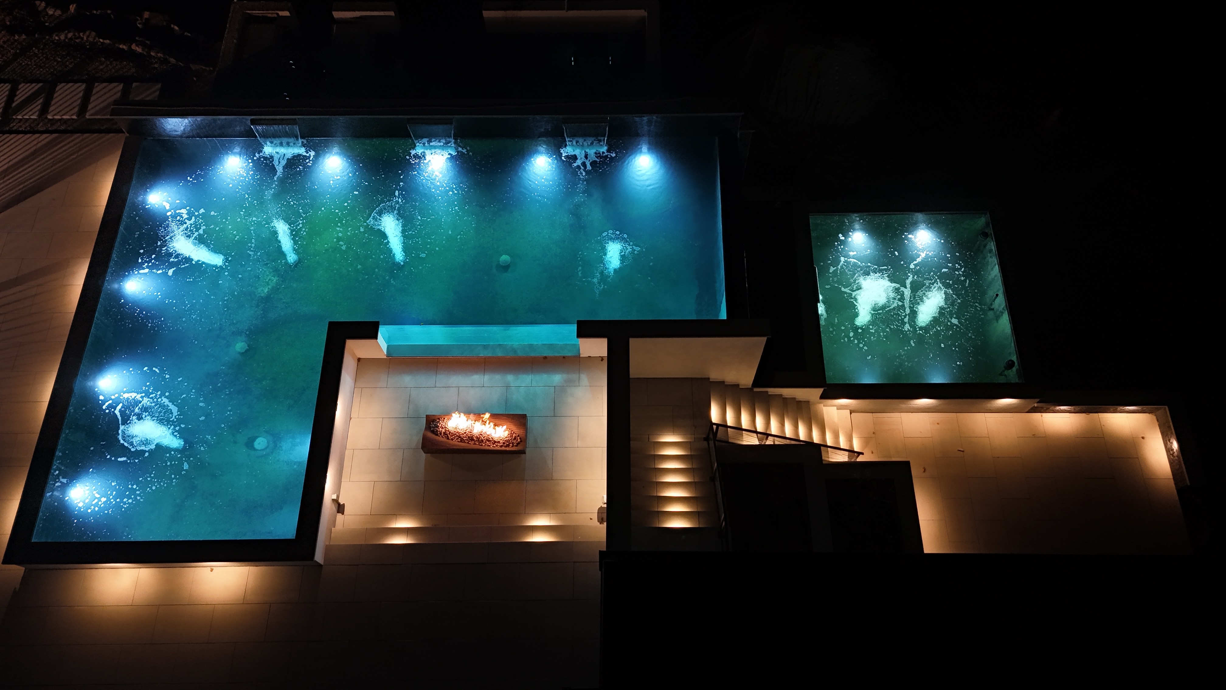 Integrated pond lighting illuminates the water, highlighting the movement of the koi and adding depth to the upper and lower ponds. Surrounding landscape lighting complements the water features, accentuating the architectural lines, stonework, and nearby plantings. Integrated pond lighting illuminates the water, highlighting the movement of the koi and adding depth to the upper and lower ponds. Surrounding landscape lighting complements the water features, accentuating the architectural lines, stonework, and nearby plantings.